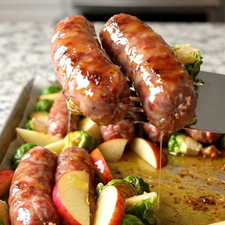 A sheet pan filled with golden-brown Italian sausage, roasted Brussels sprouts, and caramelized apple wedges.