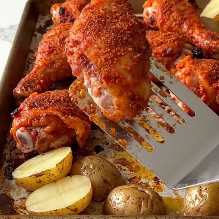 A sheet pan filled with roasted chicken drumsticks and halved baby potatoes, seasoned with a deep red spice rub.