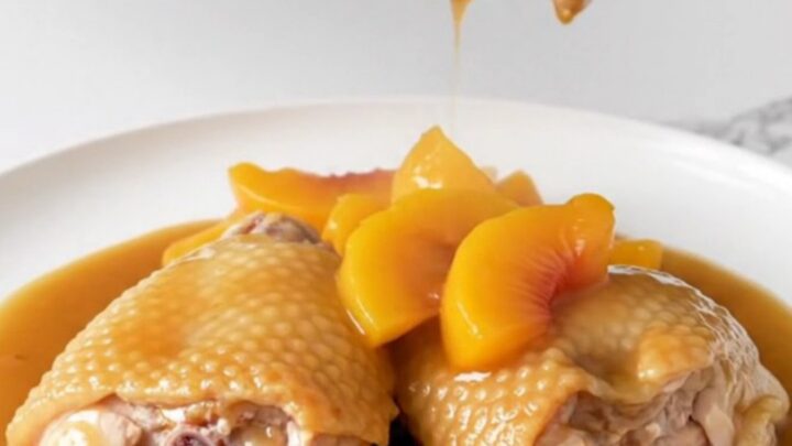 Close-up of Crockpot Peach Bourbon Chicken Thighs with a rich amber sauce and fresh peach slices.