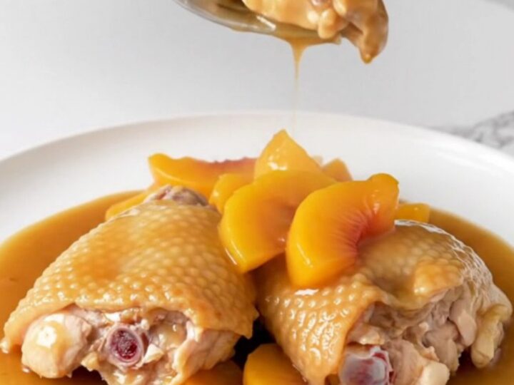 Close-up of Crockpot Peach Bourbon Chicken Thighs with a rich amber sauce and fresh peach slices.