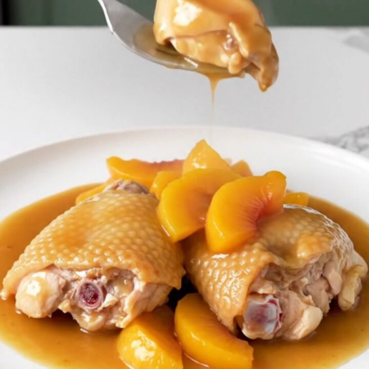 Close-up of Crockpot Peach Bourbon Chicken Thighs with a rich amber sauce and fresh peach slices.
