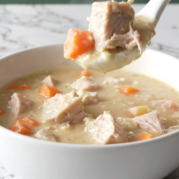 A bowl of creamy turkey and root vegetable chowder sitting on a marble counter.