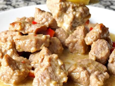 A bowl of tender, cooked pork bites in a creamy coconut sauce with pineapple and red peppers.