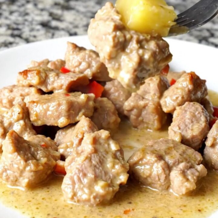 A bowl of tender, cooked pork bites in a creamy coconut sauce with pineapple and red peppers.