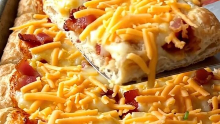 A sheet pan breakfast pizza with golden crust, eggs, bacon, and peppers.