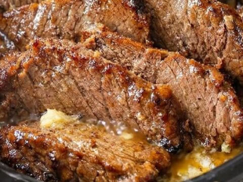 Close-up of tender, juicy slices of beef brisket in a dark slow cooker with rich garlic gravy and rising steam.