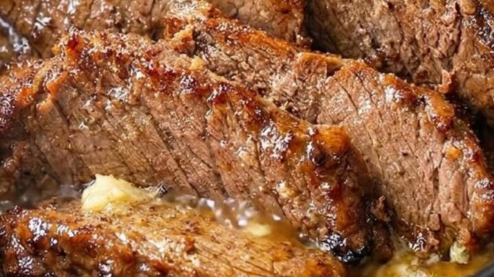 Close-up of tender, juicy slices of beef brisket in a dark slow cooker with rich garlic gravy and rising steam.