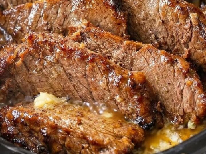Close-up of tender, juicy slices of beef brisket in a dark slow cooker with rich garlic gravy and rising steam.