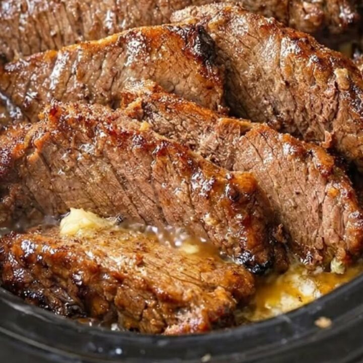 Close-up of tender, juicy slices of beef brisket in a dark slow cooker with rich garlic gravy and rising steam.