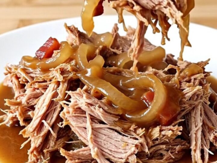 A close-up shot of shredded pork coated in a dark, glossy bacon and onion jam sauce on a white plate.