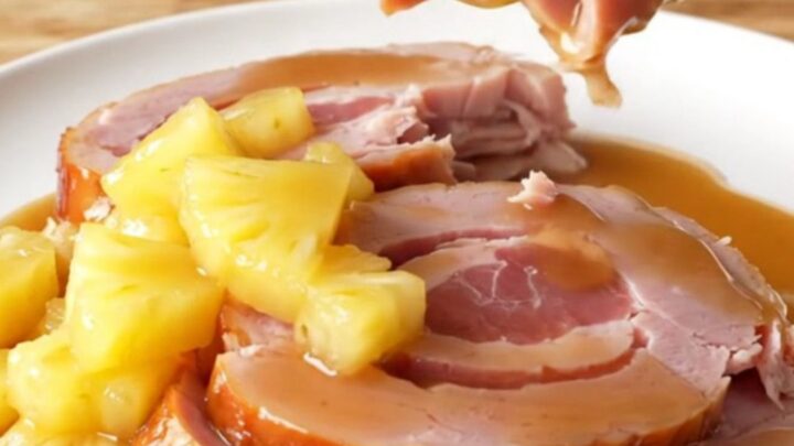 A close-up of a spiral-sliced ham in a slow cooker topped with pineapple chunks and brown sugar glaze.