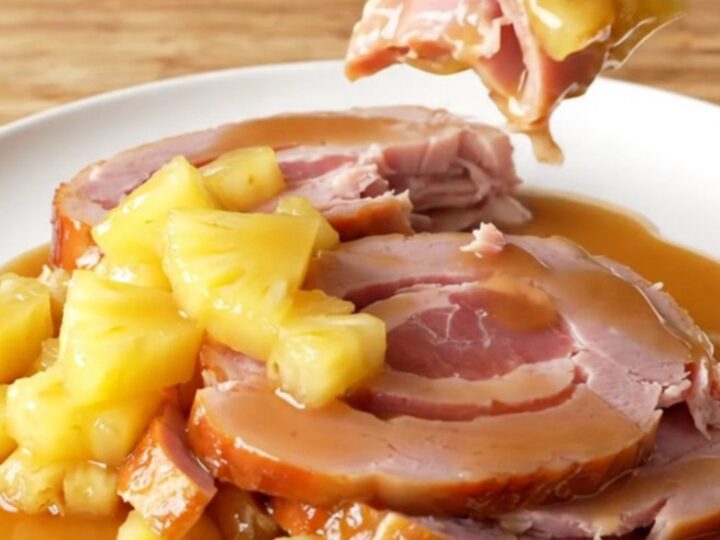 A close-up of a spiral-sliced ham in a slow cooker topped with pineapple chunks and brown sugar glaze.