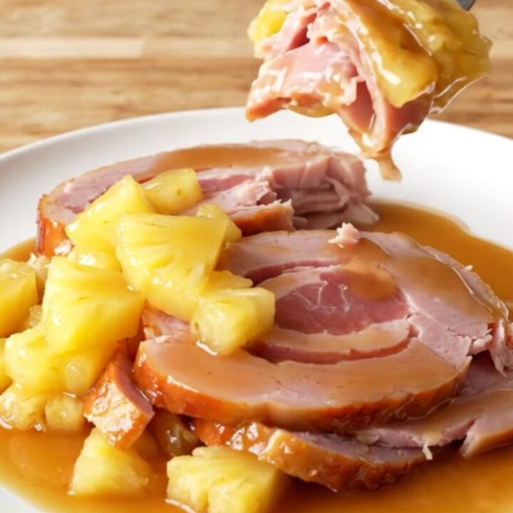 A close-up of a spiral-sliced ham in a slow cooker topped with pineapple chunks and brown sugar glaze.