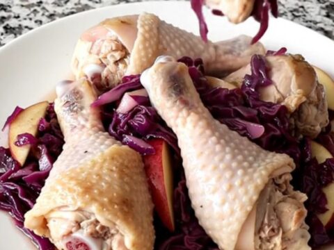 A slow cooker filled with chicken drumsticks, purple cabbage, and apple slices.