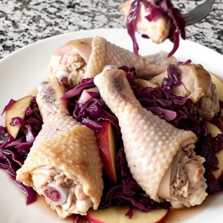 A slow cooker filled with chicken drumsticks, purple cabbage, and apple slices.