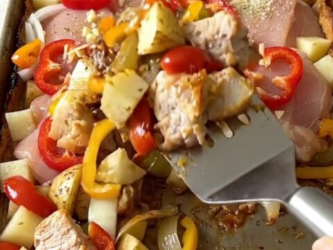 A sheet pan filled with golden-brown roasted chicken chunks, potato cubes, and cherry peppers.