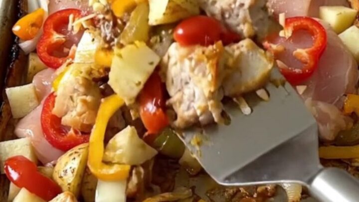 A sheet pan filled with golden-brown roasted chicken chunks, potato cubes, and cherry peppers.