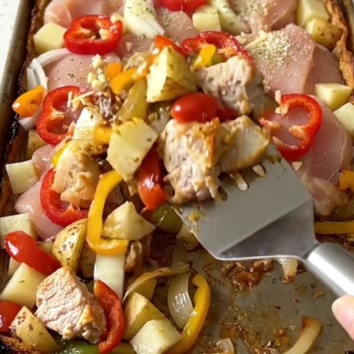 A sheet pan filled with golden-brown roasted chicken chunks, potato cubes, and cherry peppers.