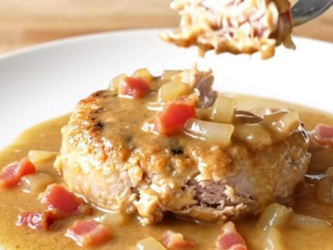 A delicious slow cooker turkey burger steak topped with creamy bacon gravy on a white plate.