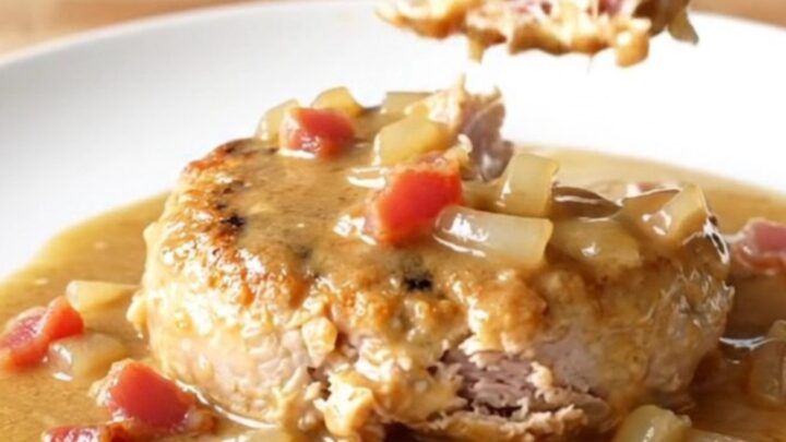 A delicious slow cooker turkey burger steak topped with creamy bacon gravy on a white plate.
