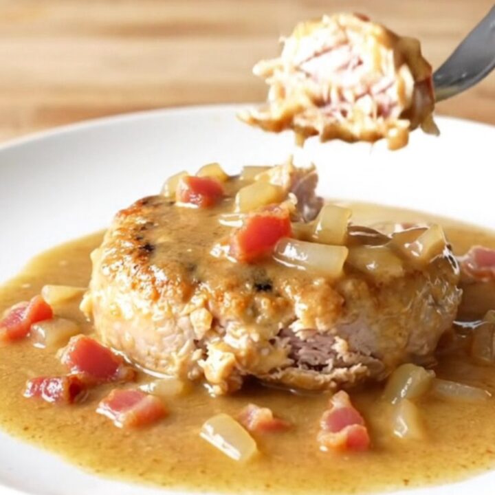A delicious slow cooker turkey burger steak topped with creamy bacon gravy on a white plate.