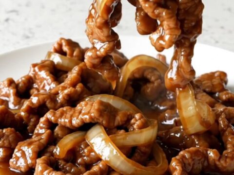 A bowl of tender Crockpot Pork Bulgogi served over white rice with sesame seeds and onions.