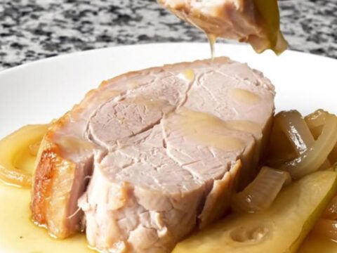 A plate featuring a tender, cooked pork loin slice topped with soft pear wedges and onions in a light sauce.
