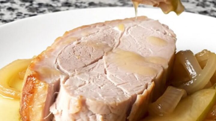 A plate featuring a tender, cooked pork loin slice topped with soft pear wedges and onions in a light sauce.