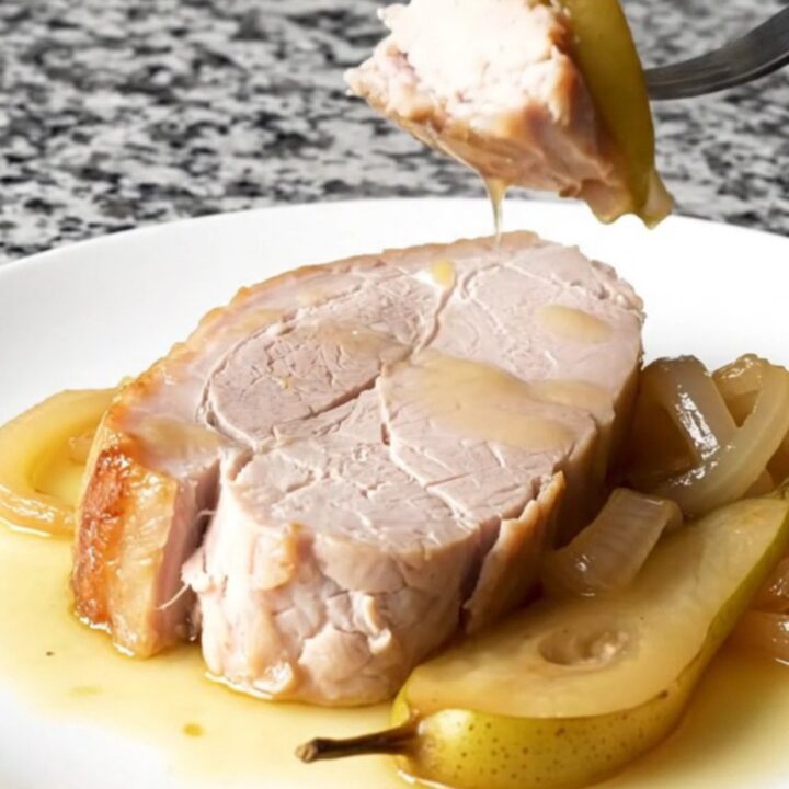 A plate featuring a tender, cooked pork loin slice topped with soft pear wedges and onions in a light sauce.