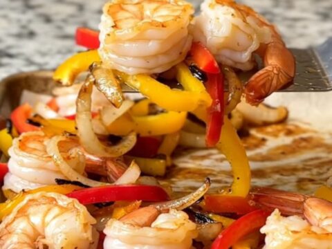 A sheet pan filled with roasted shrimp, colorful bell pepper strips, and onions, all seasoned and ready to serve.