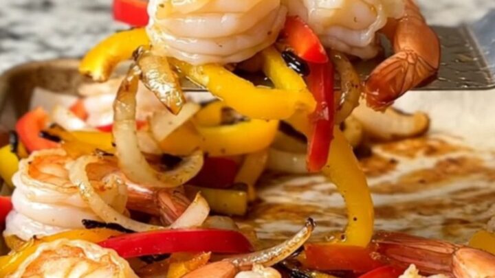 A sheet pan filled with roasted shrimp, colorful bell pepper strips, and onions, all seasoned and ready to serve.