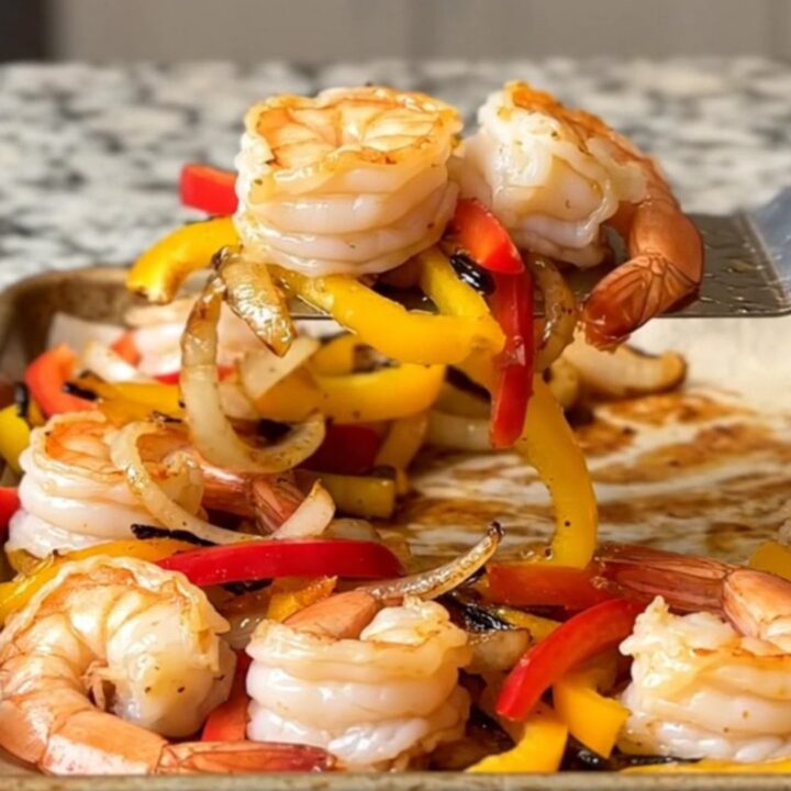 A sheet pan filled with roasted shrimp, colorful bell pepper strips, and onions, all seasoned and ready to serve.