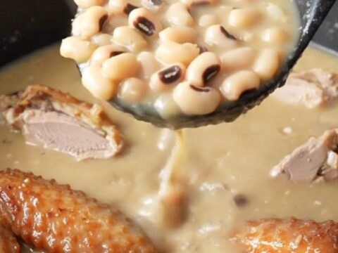 A close-up of a bowl of creamy swamp soup filled with smoked turkey wings, black-eyed peas, and turnip greens.