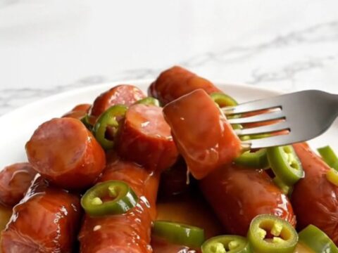 A top-down view of a slow cooker filled with sliced kielbasa and baby potatoes glazed in a glossy amber syrup.