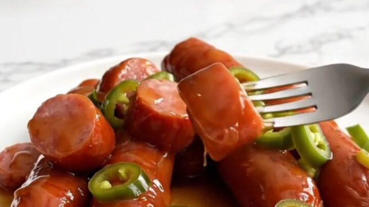 A top-down view of a slow cooker filled with sliced kielbasa and baby potatoes glazed in a glossy amber syrup.