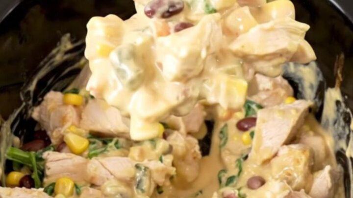 A warm, creamy Southwest chicken dip in a slow cooker, topped with black beans, corn, and spinach.