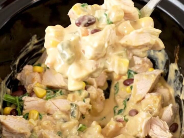 A warm, creamy Southwest chicken dip in a slow cooker, topped with black beans, corn, and spinach.