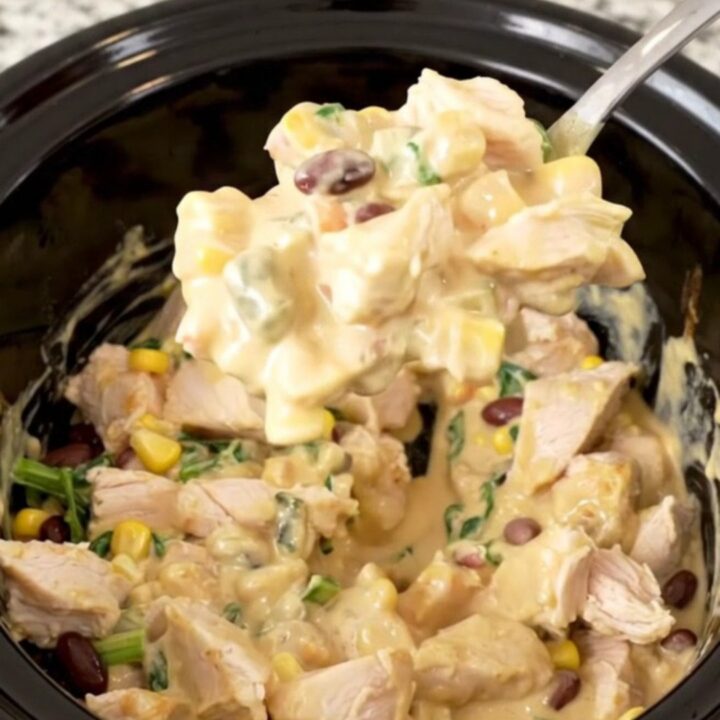A warm, creamy Southwest chicken dip in a slow cooker, topped with black beans, corn, and spinach.