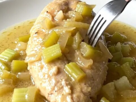 A close-up shot of cooked chicken breast smothered in a creamy celery sauce on a white plate.