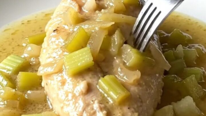 A close-up shot of cooked chicken breast smothered in a creamy celery sauce on a white plate.