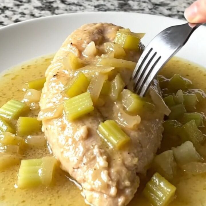 A close-up shot of cooked chicken breast smothered in a creamy celery sauce on a white plate.