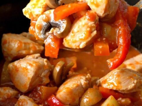 A rustic, close-up shot of slow-cooked chicken cacciatore stew in a black stoneware insert, showing tender chicken, peppers