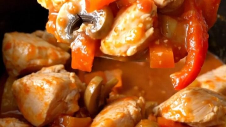 A rustic, close-up shot of slow-cooked chicken cacciatore stew in a black stoneware insert, showing tender chicken, peppers