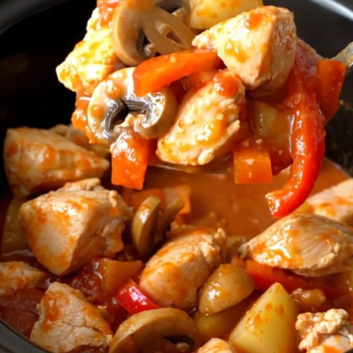 A rustic, close-up shot of slow-cooked chicken cacciatore stew in a black stoneware insert, showing tender chicken, peppers