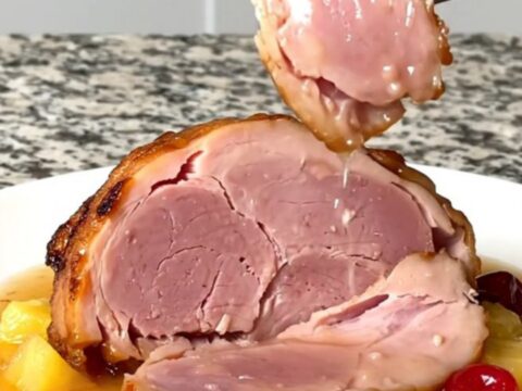 A close-up of a tender, sliced bone-in ham topped with pineapple chunks and red cherries in a glossy glaze.