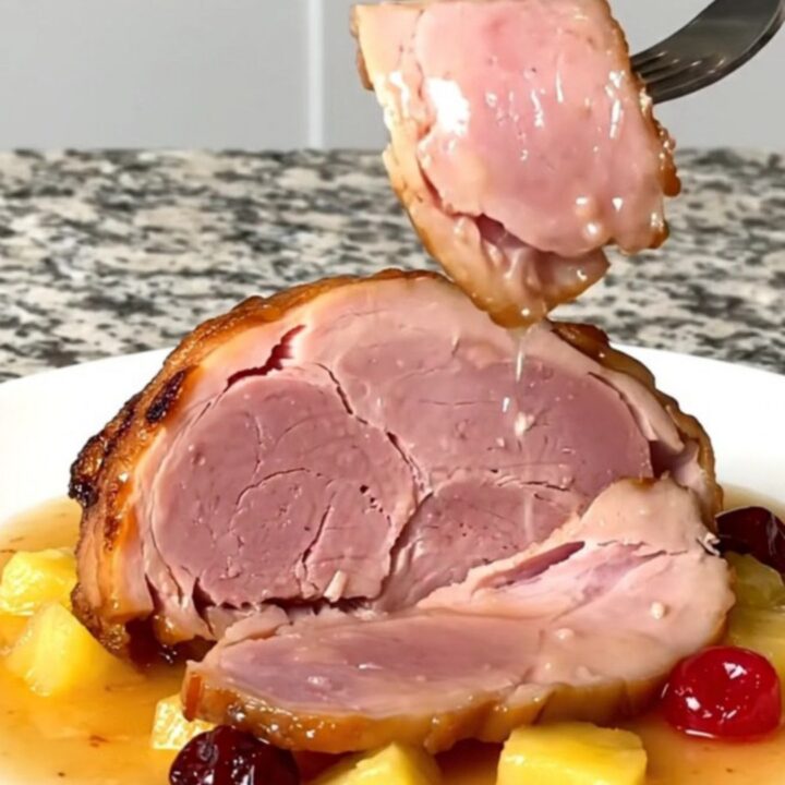 A close-up of a tender, sliced bone-in ham topped with pineapple chunks and red cherries in a glossy glaze.