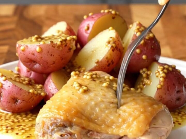 A close-up of a perfectly cooked chicken thigh and red potatoes in a creamy mustard sauce on a white plate.