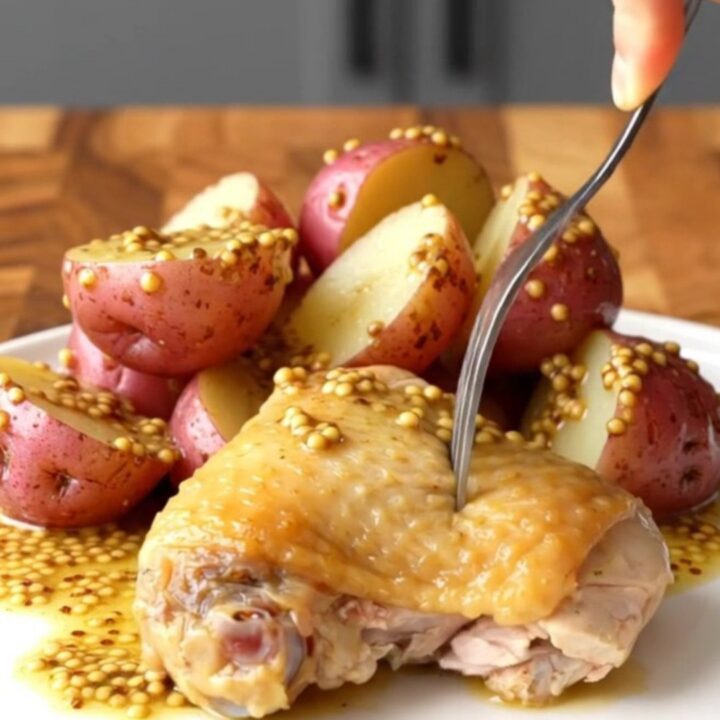 A close-up of a perfectly cooked chicken thigh and red potatoes in a creamy mustard sauce on a white plate.