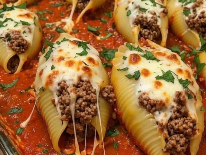 A glass baking dish filled with golden-brown, cheesy stuffed shells garnished with fresh green herbs.