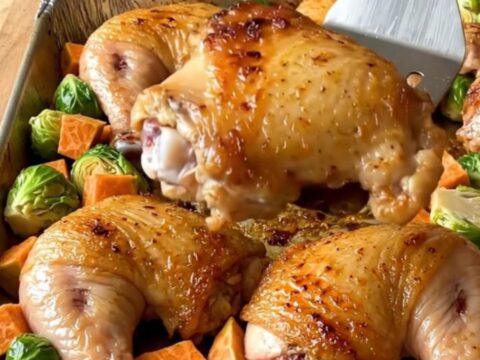 A sheet pan filled with golden-brown roasted chicken thighs, halved Brussels sprouts, and roasted sweet potato cubes.